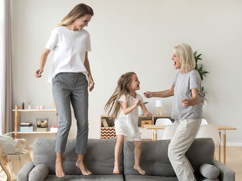 a mom, daughter and grandmom jumping on couch
